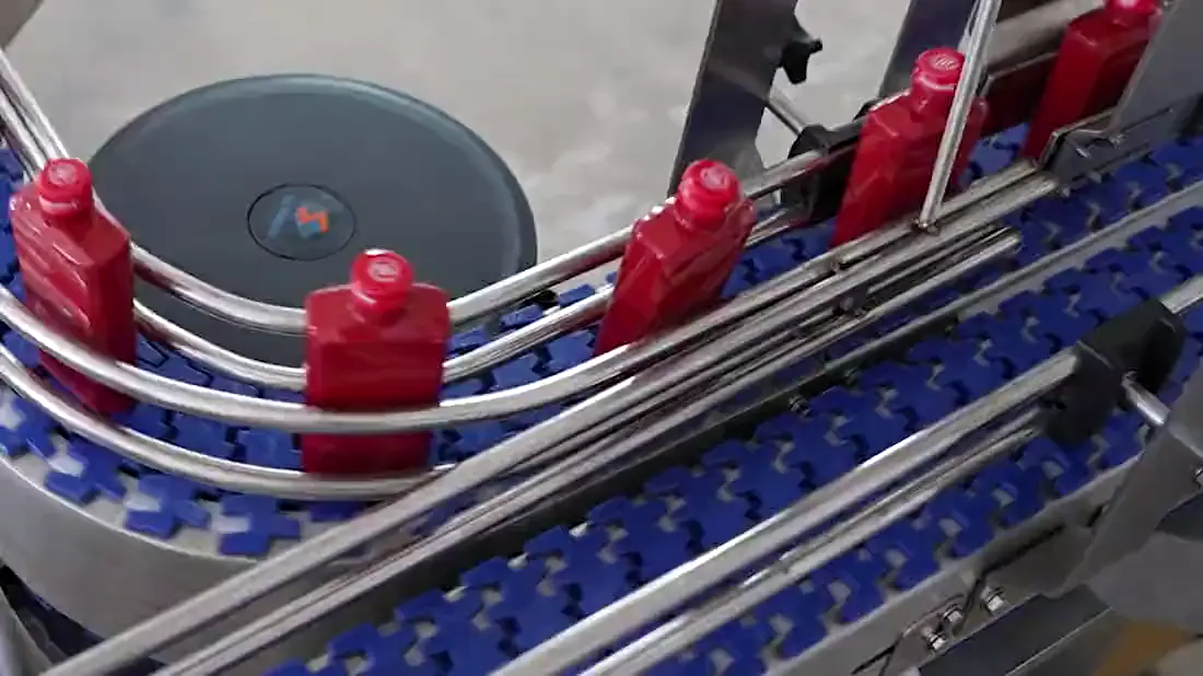 Red bottles held in guide rails on a blue modular belt, turning a curve